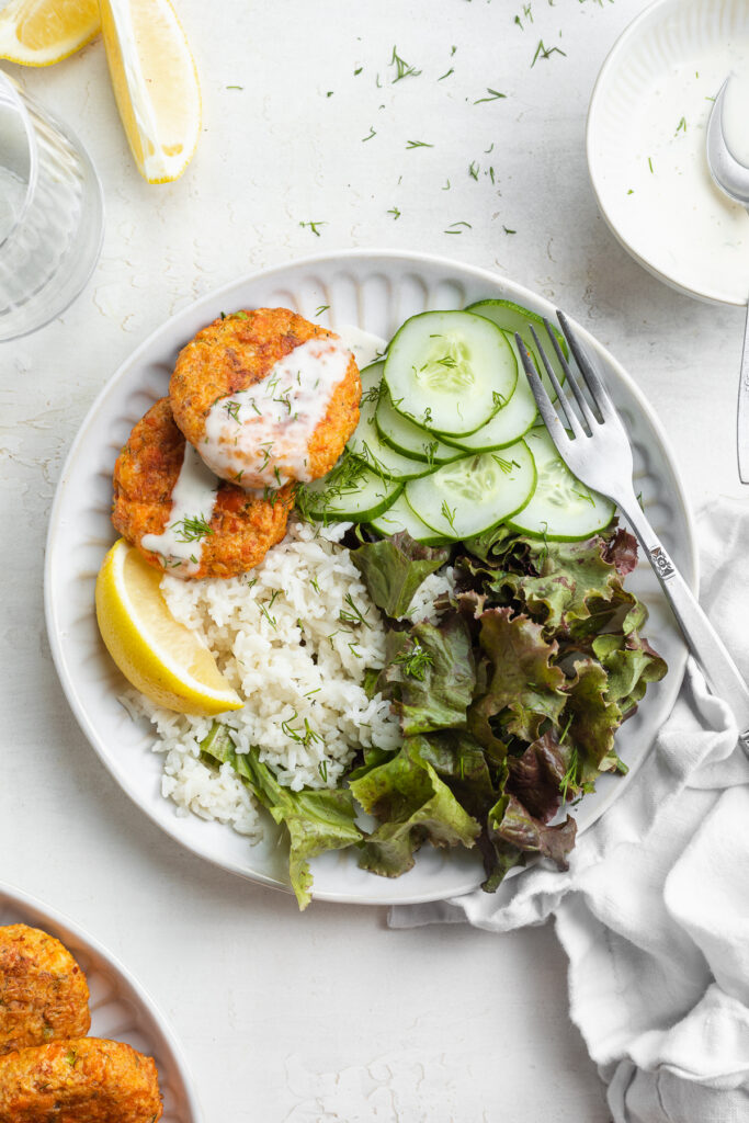 Overhead image of air fryer salmon patties on a plate over rice and lettuce with creamy dill sauce on top.