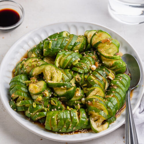 asian cucumber salad on a plate with sriracha on the side