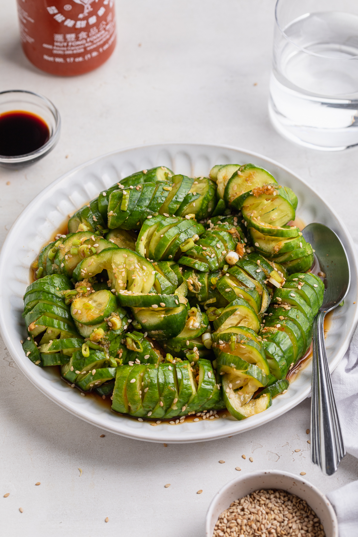 asian cucumber salad on a plate with sriracha on the side