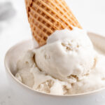 close up image of vegan vanilla ice cream in a bowl with a cone on top