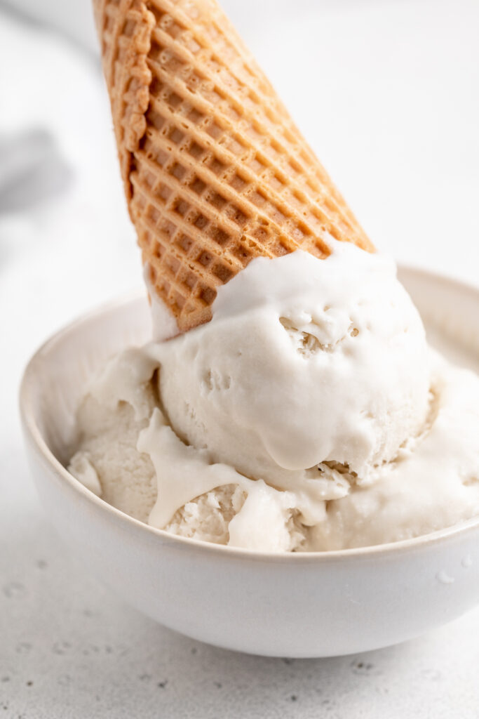 close up image of vegan vanilla ice cream in a bowl with a cone on top