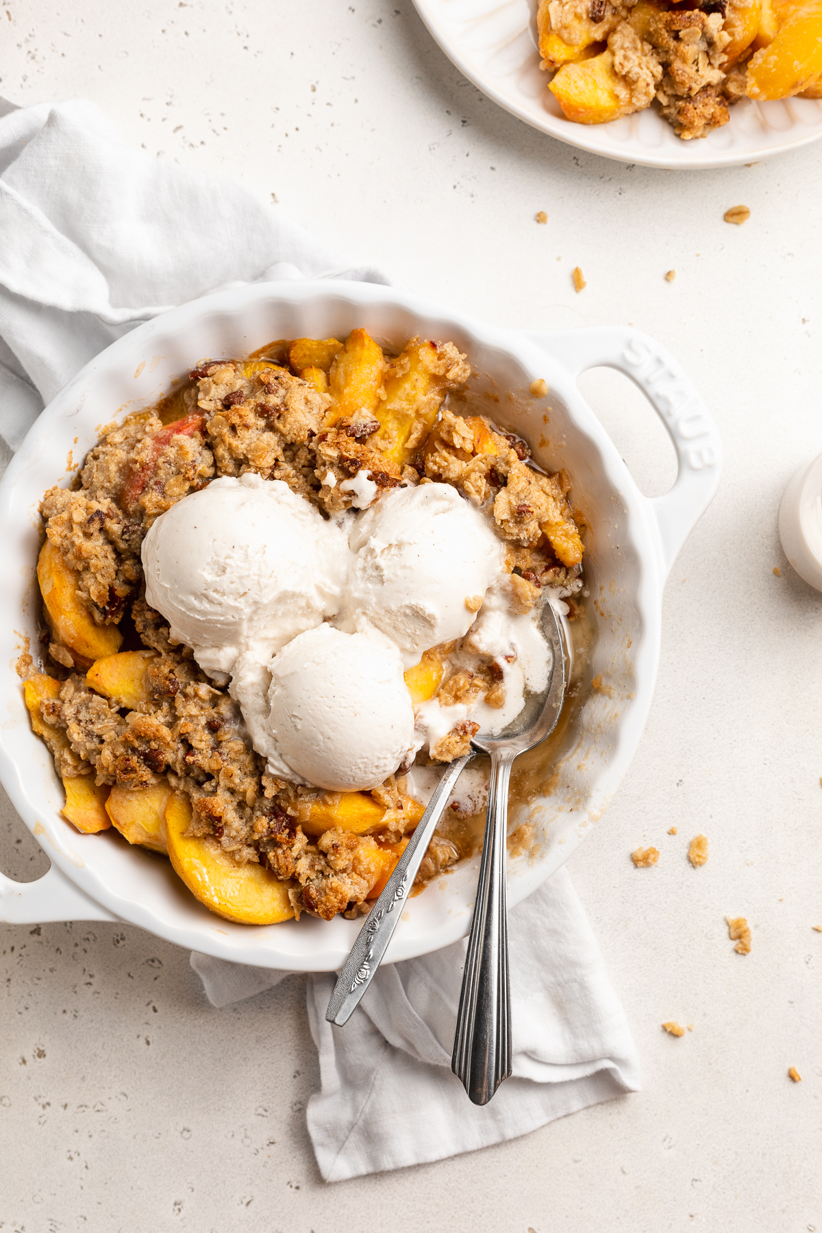overhead image of peach crisp in a pie dish wtih vanilla ice cream on top.