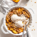 overhead image of peach crisp in a pie dish with ice cream on top and milk on the side.