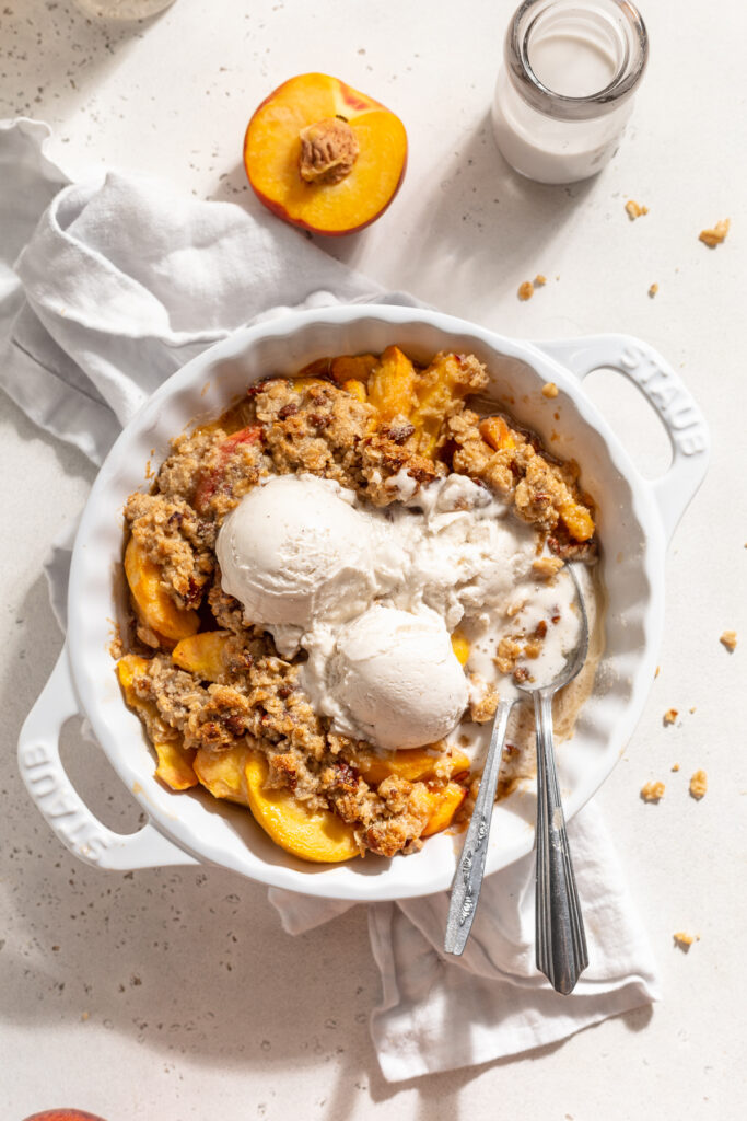 overhead image of peach crisp in a pie dish with ice cream on top and milk on the side.