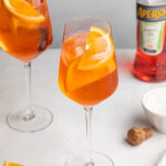 Two aperol spritz in white wine glasses with a bottle of aperol on the side.