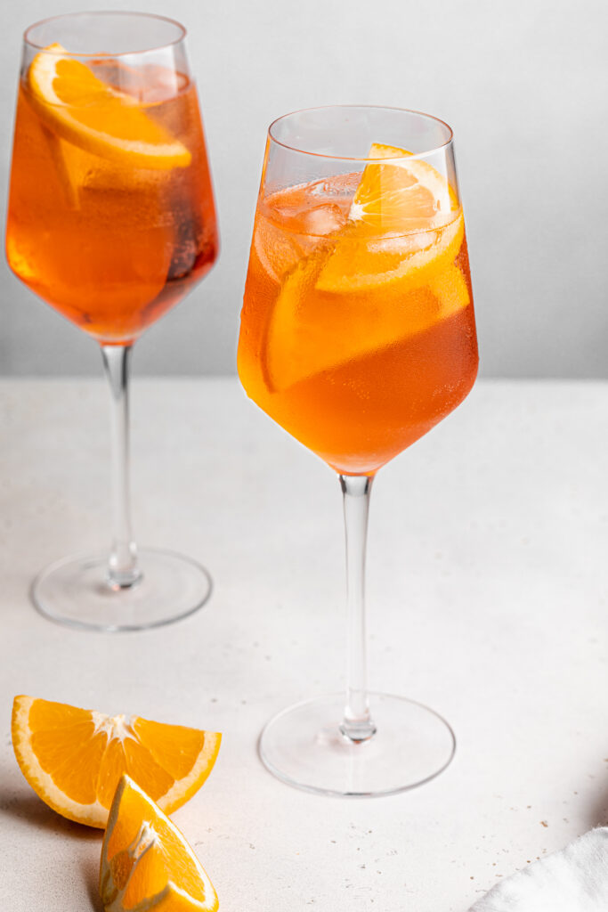 two aperol spritz with orange slices on the side.