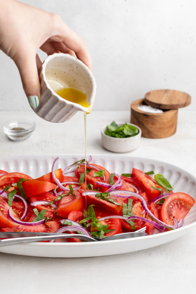 olive oil being poured over tomato salad.