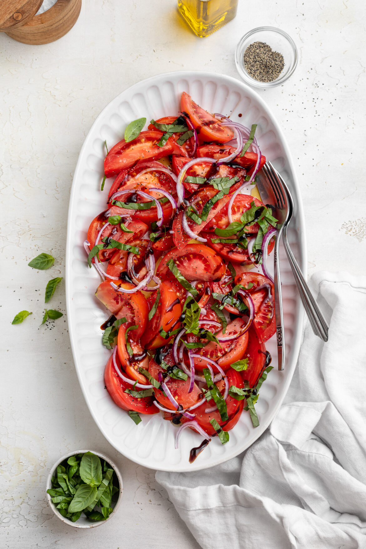 Simple Tomato Salad overhead image of tomato salad on a serving platter with olive oil and fresh basil on the side.