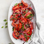overhead image of tomato salad on a serving platter with olive oil and fresh basil on the side.