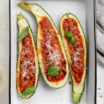 close up image of stuffed zucchini boats in a baking dish with fresh basil on top.