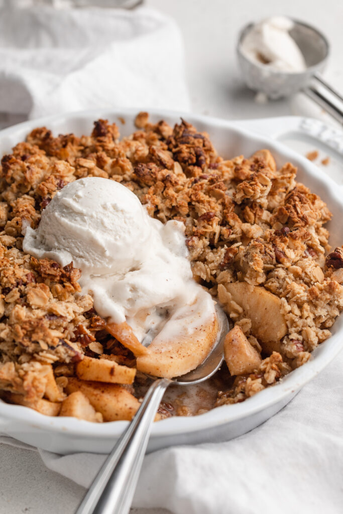 close-up image of gluten-free apple crisp in a pie dish with a spoon in it.