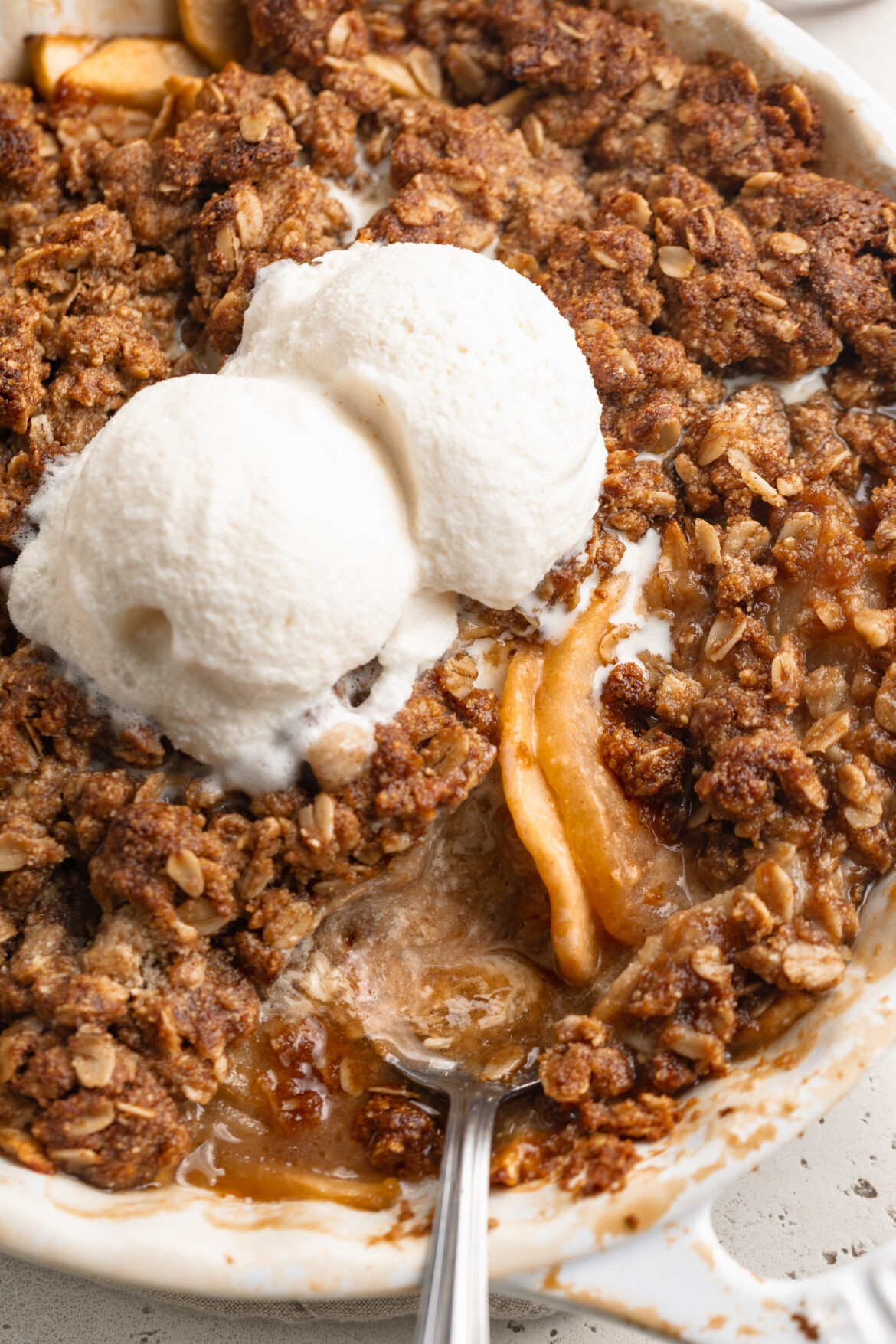 Healthy Gluten Free Apple Crisp gluten free apple crisp in a baking dish with a spoon and two scoops of ice cream on top.