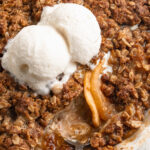 gluten free apple crisp in a baking dish with a spoon and two scoops of ice cream on top.