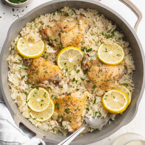 overhead image of chicken and rice in a pan with lemon slices on top.