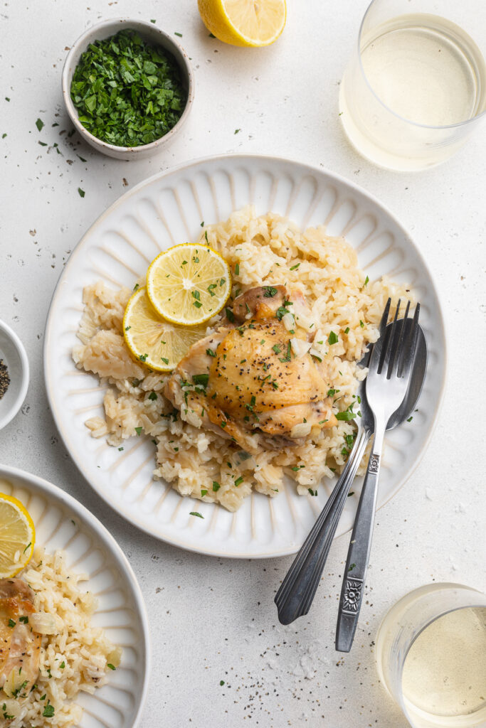 overhead image of chicken and rice on a plate with lemon, parsley, and white wine on the side.