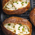 air fryer baked potato in an air fryer basket with butter and chives on top.