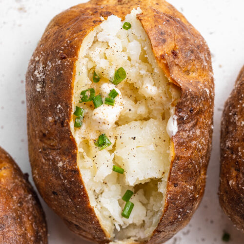 close-up overhead image of an air fryer baked potato with butter and chives on top.
