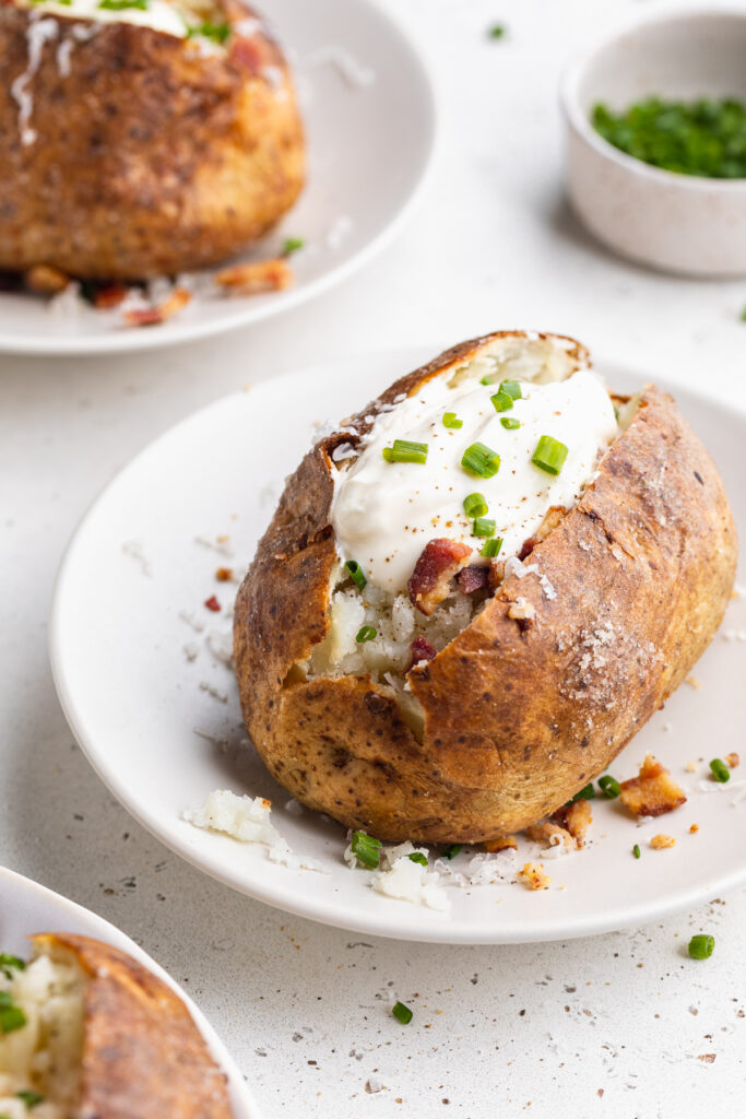 a loaded air fryer baked potato with sour cream, bacon, and chives on top.