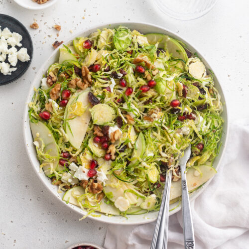 overhead image of brussels sprout salad with walnuts, pomegranate seeds, and goat cheese on the side.