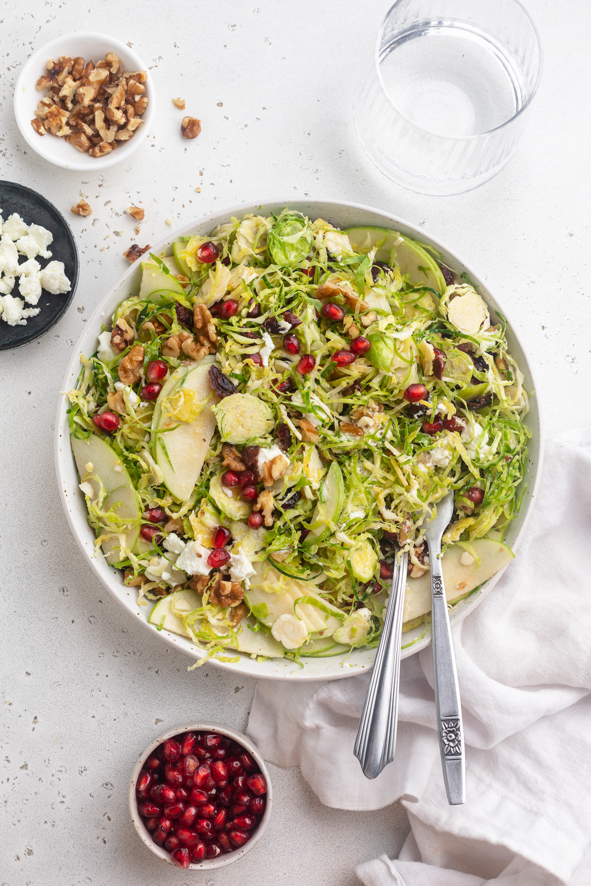 overhead image of brussels sprout salad with walnuts, pomegranate seeds, and goat cheese on the side.