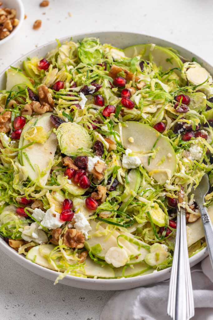 brussels sprout salad in a a bowl with serving utensils.