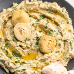 close-up image of spinach artichoke hummus with artichoke hearts on top.