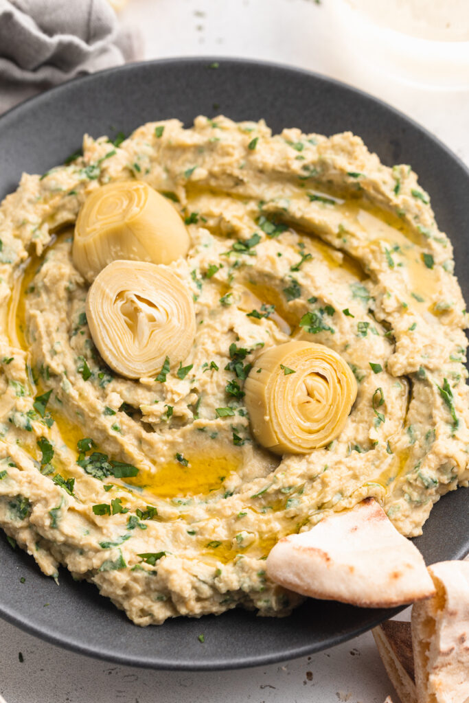 close-up image of spinach artichoke hummus with artichoke hearts on top.
