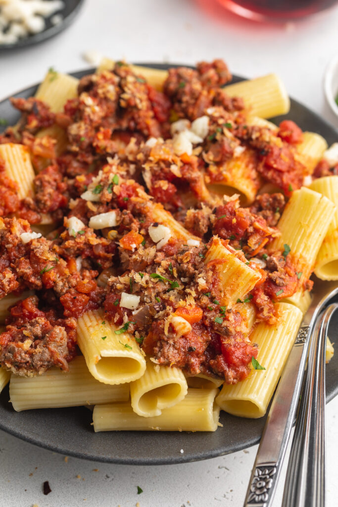 rigatoni bolognese on a plate with a fork and spoon.