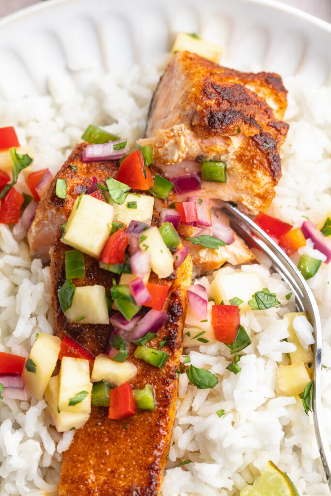 close-up image of blackened salmon served over coconut rice with pineapple salsa on top.
