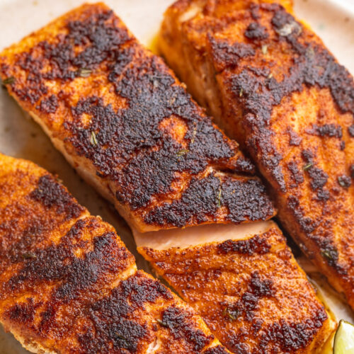 close-up image of three blackened salmon fillets on a plate.