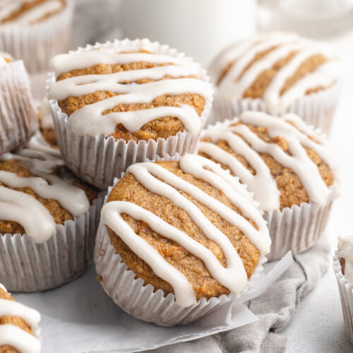 healthy carrot cake muffins with cream cheese icing on top, stacked on top of each other.