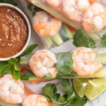 close-up overhead image of shrimp spring rolls on a plate with peanut sauce.