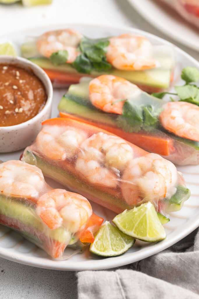 shrimp spring rolls on a plate with peanut sauce and fresh limes on the side.