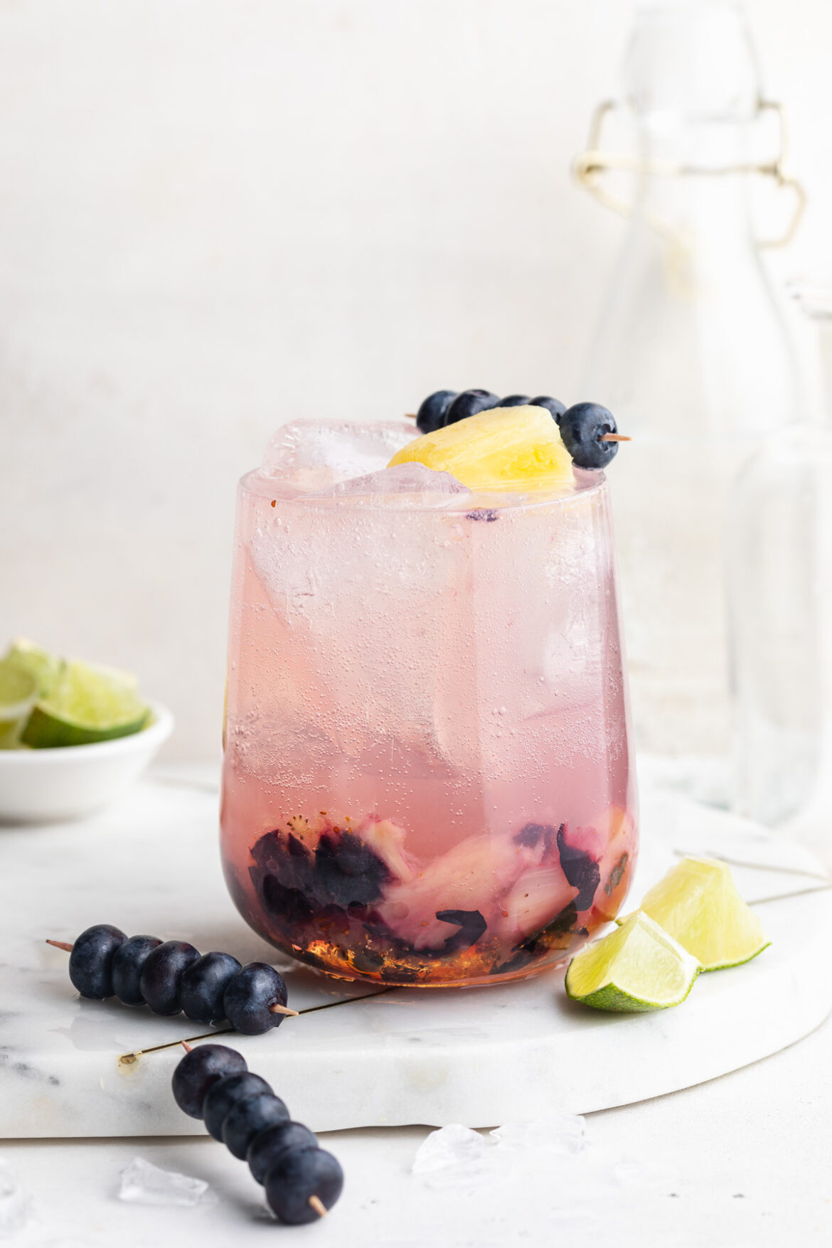 Sunset Spritz Mocktail Recipe sunset spritz mocktail in a glass with fresh blueberries and pineapple on top.