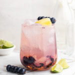 sunset spritz mocktail in a glass with fresh blueberries and pineapple on top.