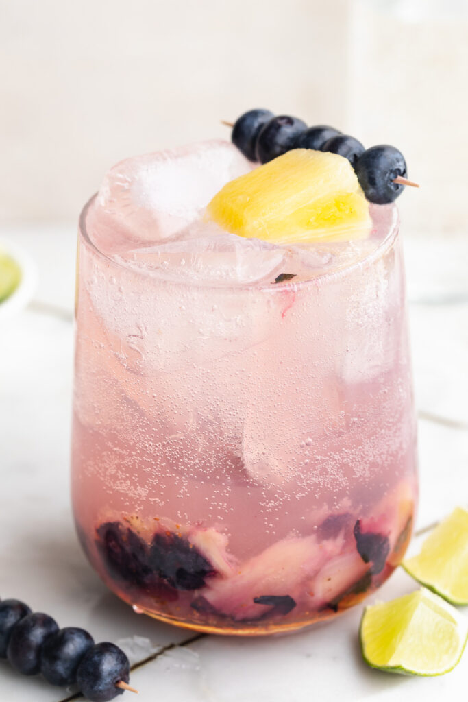 close-up image of sunset spritz mocktail with fresh bleuberries and pineapple on top.