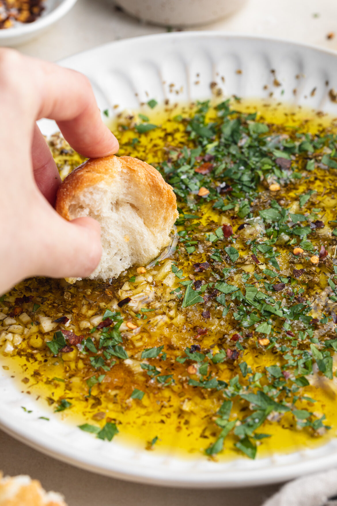 Garlic and Herb Olive Oil Dip bread being dipped into garlic and herb olive oil dip.