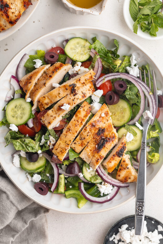 overhead image of mediterranean grilled chicken salad in a bowl with fresh mint on the side.