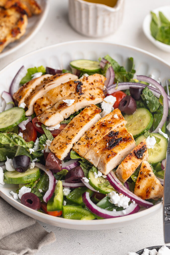 mediterranean grilled chicken salad in a bowl with lemon dijon dressing on the side.