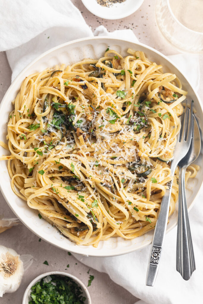 close-up overhead image of pasta with caramelized zucchini in a bowl with parsley and parmesan cheese on top.
