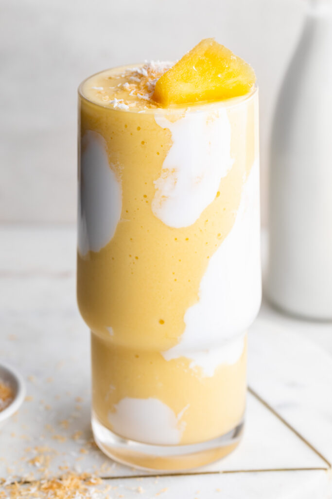 mango pineapple smoothie with pineapple on top and toasted coconut on the side.