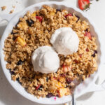 Overhead image of summer fruit crisp in a baking dish with vanilla ice cream on top.