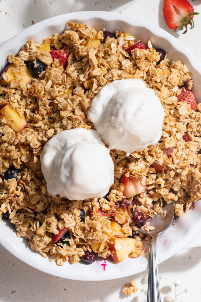 Close-up overhead image of summer fruit crisp in a baking dish with vanilla ice cream on top.