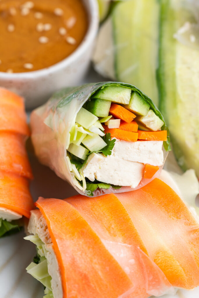 summer roll sliced in half on a plate, with cucumber, carrots, and tofu inside.