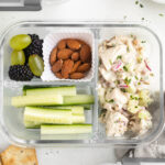 overhead image of chicken salad lunch boxes with cucumbers, almond, grapes, and blackberries