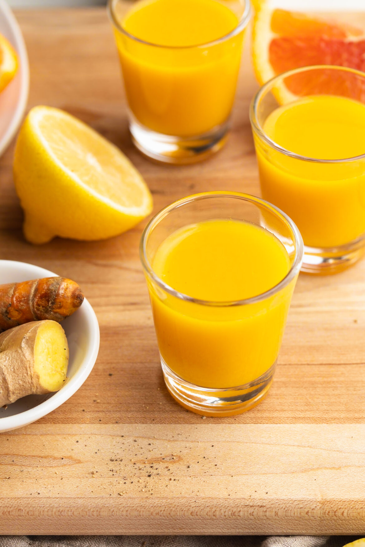 Homemade Ginger and Turmeric Immunity Shots Recipe Homemade immunity shots with fresh lemon, orange, ginger, and turmeric on the side.