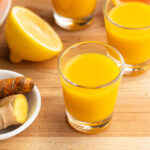 Homemade immunity shots with fresh lemon, orange, ginger, and turmeric on the side.