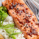 Close up image of a honey teriyaki salmon fillet on a plate with rice and sliced green onion.