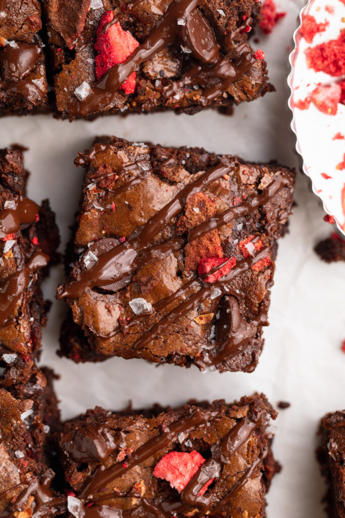 overhead image of chocolate covered strawberry almond flour brownies with a chocolate drizzle and freeze dried strawberries on top.