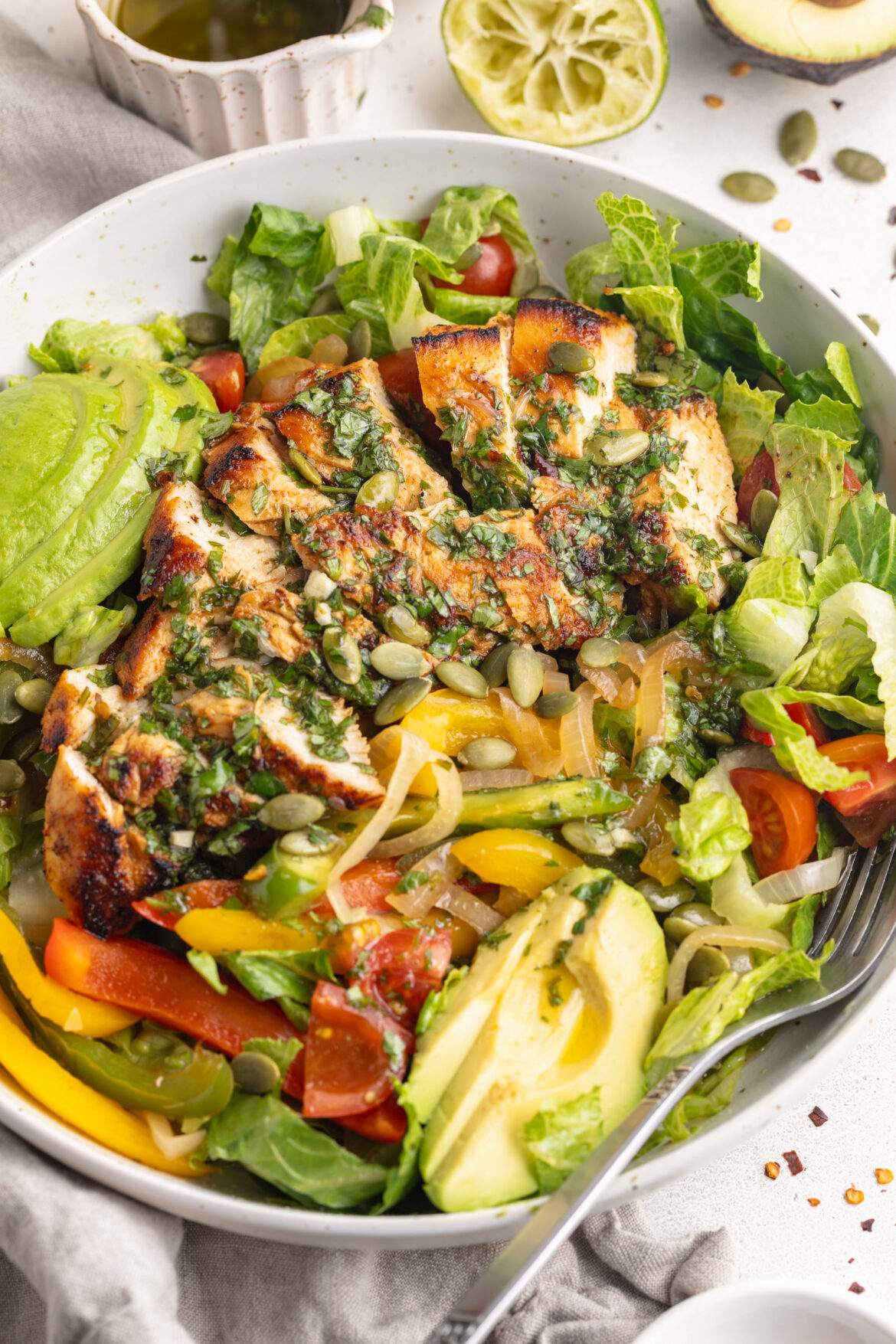 Chicken Fajita Salad with Cilantro-Lime Dressing chicken fajita salad in a bowl with cilantro lime dressing on top and on the side.
